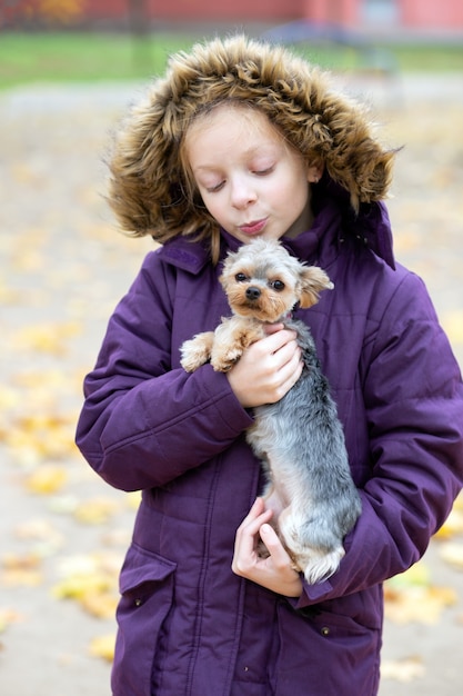 Cute girl in a purple jacket holds a Yorkshire Terrier dog