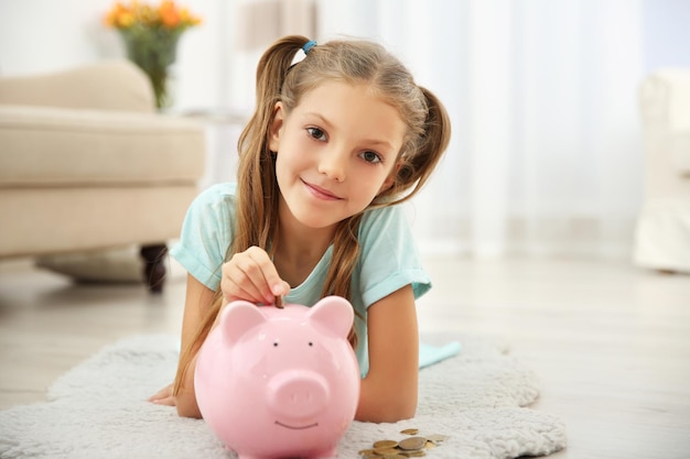 Cute girl putting coins into piggy bank at home