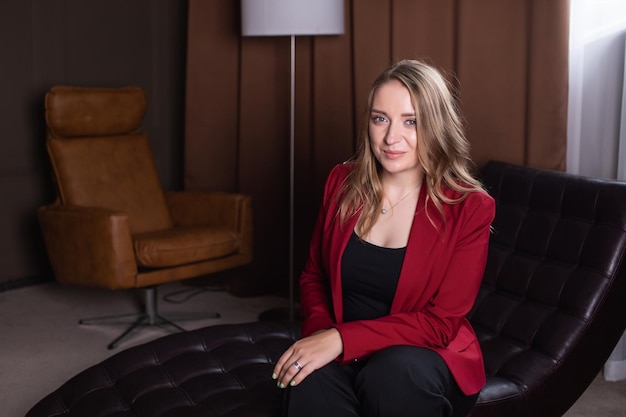 A cute girl in a red jacket is sitting on a couch in the psychologist's office