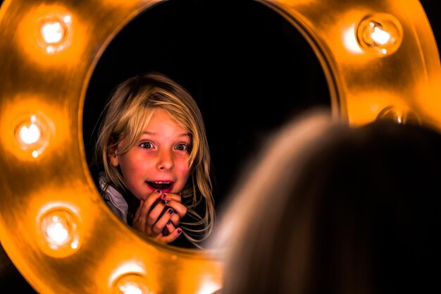 Cute girl reflecting in illuminated mirror