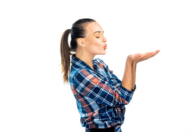 Cute girl sends a kiss Adorable young girl holds hands near lips in kiss sign Checkered shirt photo from the side