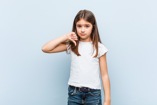 Cute girl showing a dislike gesture, thumbs down. Disagreement concept.