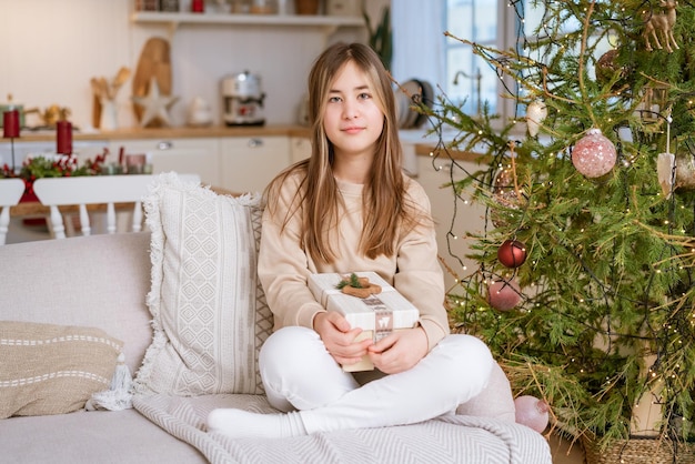 A cute girl sits on the couch with a christmas present from her family