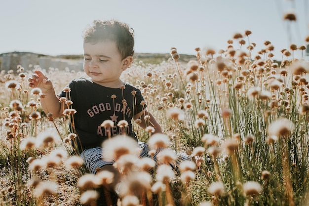 cute girl sitting amidst flowers against sky