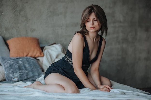 Cute girl sitting on bed in morning in black lingerie