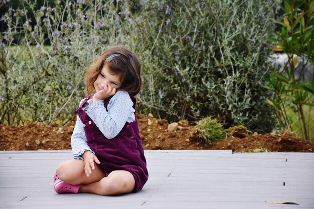 Photo cute girl sitting on boardwalk against plants