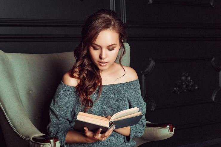 Фотография милая девушка сидит в кресле и читает книгу в офисе