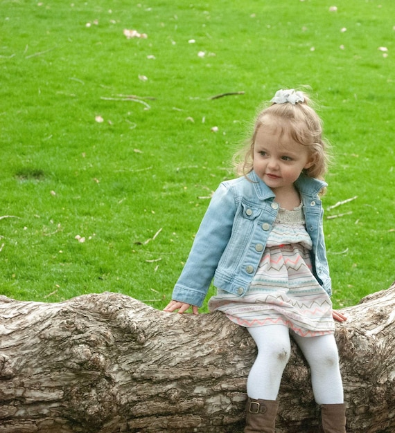 Photo cute girl sitting on fallen tree at park