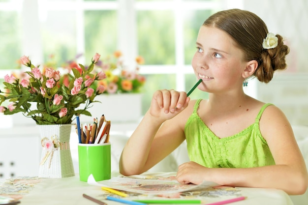 Cute girl sitting at table and drawing with pencils