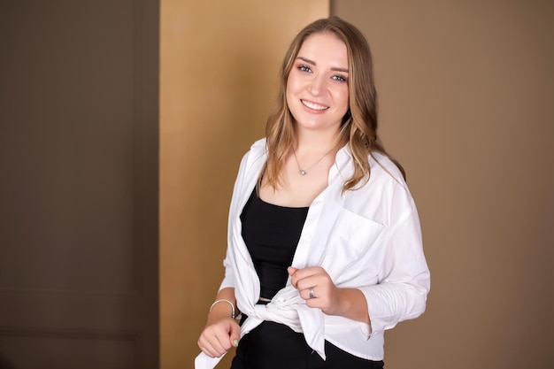 A cute girl stands and adjusts the ends of a white shirt