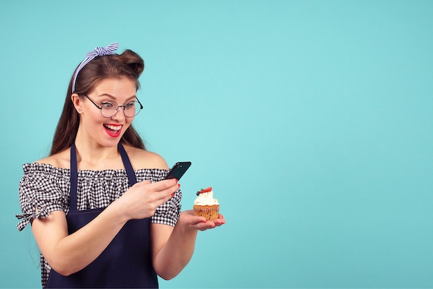 Cute girl takes a cupcake in hand on blue background in Studio