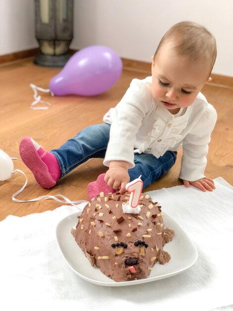 Foto ragazza carina che tocca la torta di compleanno in un piatto sul pavimento