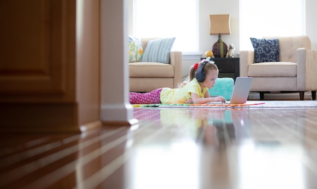 Photo cute girl using laptop while lying down on floor