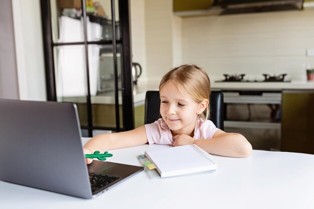 Photo cute girl using laptop while sitting by table at home
