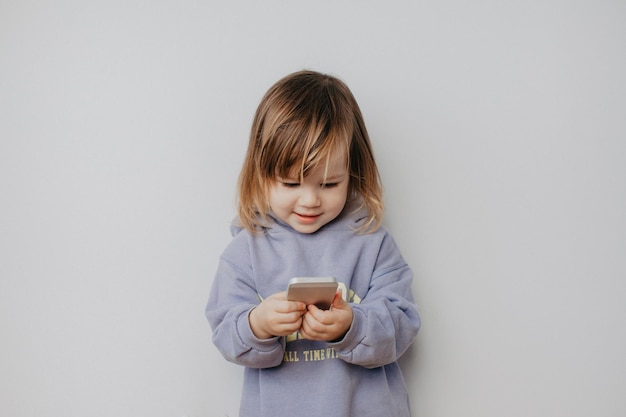 Photo cute girl using smart phone standing against wall