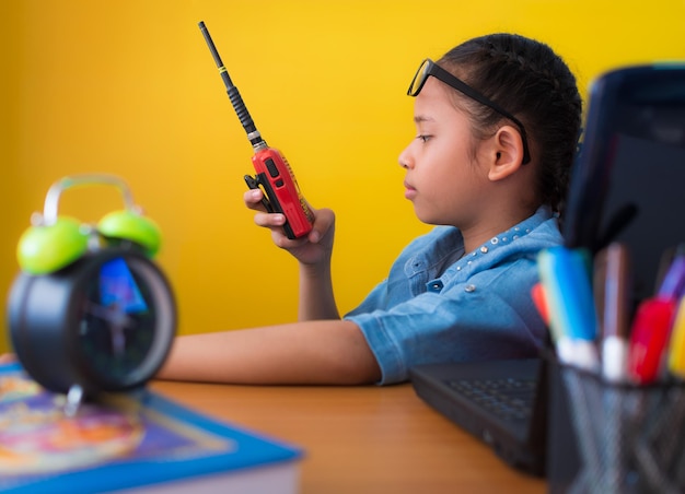 cute girl using walkie - talkie at working desk with laptop isolated yellow background