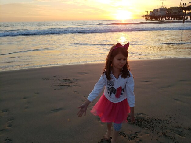 Foto ragazza carina che cammina sulla spiaggia contro il cielo durante il tramonto