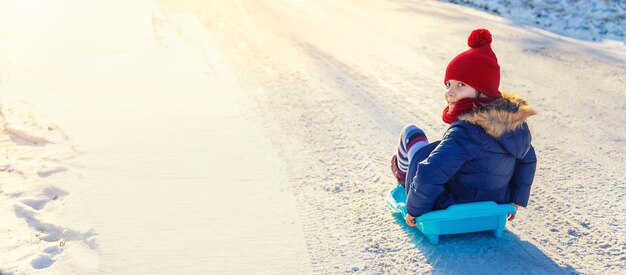 Photo cute girl in warm clothing sledding on snow