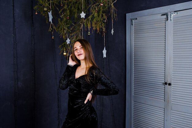 Foto usura sveglia della ragazza sul vestito nero contro la decorazione di natale.