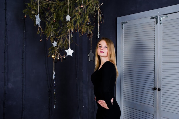 Foto usura sveglia della ragazza sul vestito nero contro la decorazione di natale.