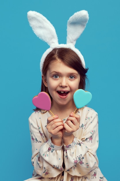 Cute girl wearing easter bunny ears having two cookies in heart shape