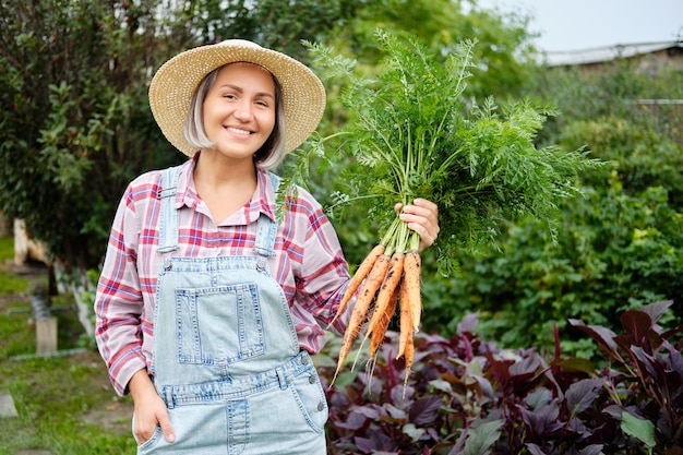 Cute girl in wearing Hat Picking Carrots in a Garden. Autumn Vegetable Harvest