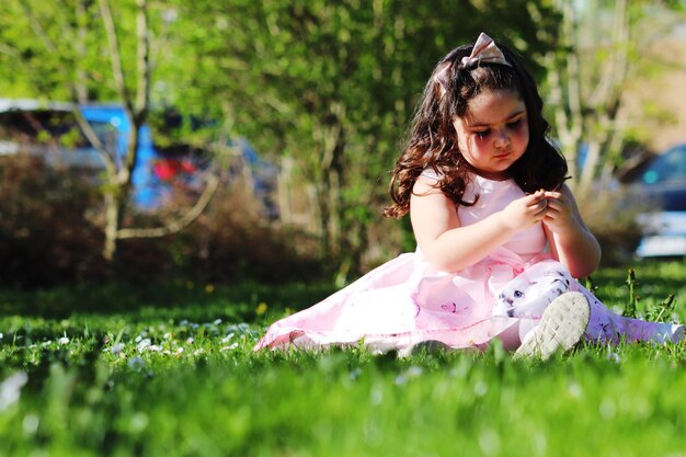 Photo cute girl wearing pink dress sitting on grassy field in park