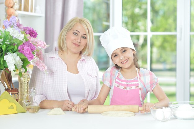 Cute girl in white hat with her mother making dough