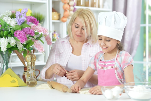 Милая девушка в белой шляпе со своей матерью делает тесто