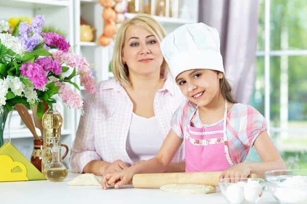 Cute girl in white hat with her mother making dough