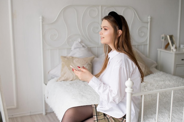 A cute girl in a white shirt and a red manicure holds a phone and smiles