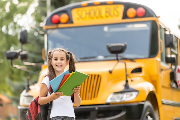 Ragazza carina con uno zaino in piedi vicino all'autobus che va a scuola in posa per il primo piano pensieroso della fotocamera