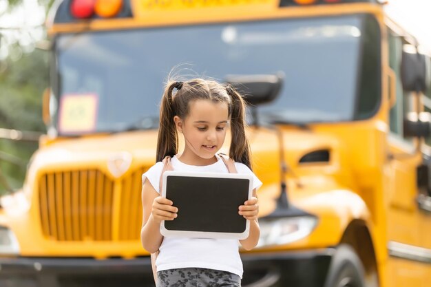 カメラの物思いにふけるクローズアップにポーズをとって学校に行くバスの近くに立っているバックパックを持つかわいい女の子