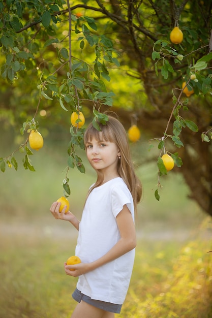 A cute girl with blond hair in a white T-shirt with summer lemons in the garden under a tree