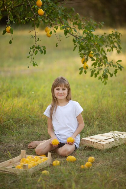 A cute girl with blond hair in a white T-shirt with summer lemons in the garden under a tree