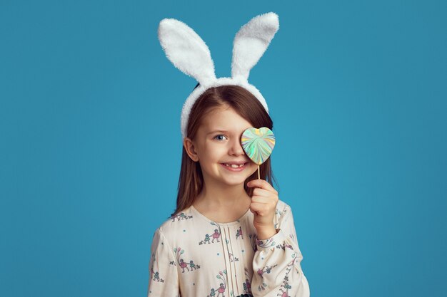 Cute girl with bunny ears hiding her eye behind a cookie in shape of heart