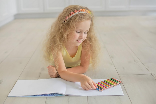 a cute girl with curly hair and blue eyes draws in an album with colored pencils