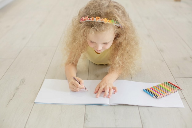 Una ragazza carina con i capelli ricci e gli occhi azzurri disegna un album con matite colorate