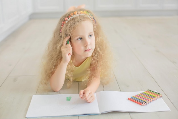 a cute girl with curly hair and blue eyes draws in an album with colored pencils