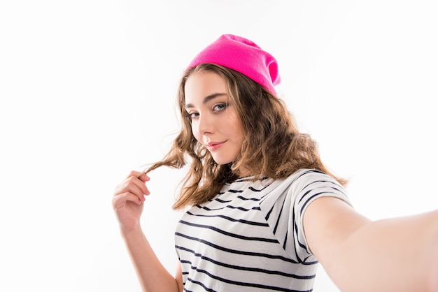 Cute girl with curly hair in pink cap making selfie