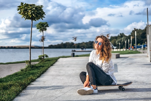 Ragazza carina con i capelli ricci con skateboard nel parco