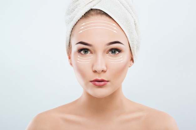 Cute girl with dark eyebrows and naked shoulders, wearing white towel on head,  looking at camera,, a model with light nude make-up, white studio background, beauty photo, front view.