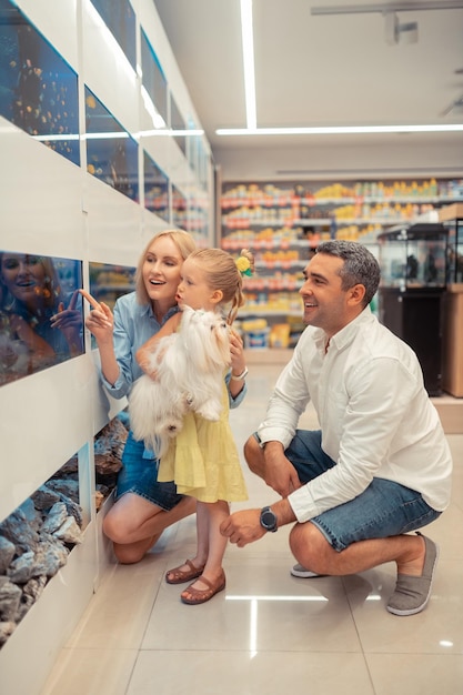 Cute girl with dog in hands visiting aquarium with parents