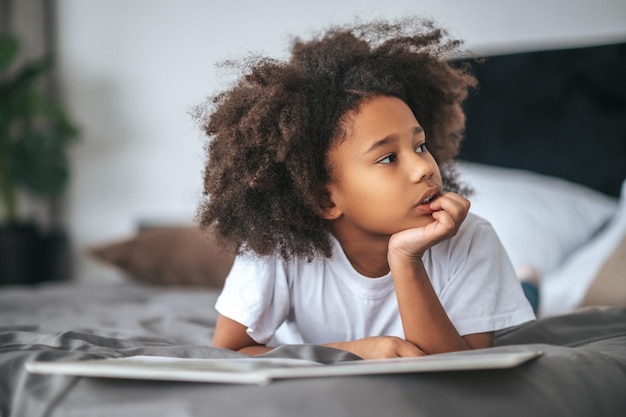 A cute girl with hair band lying on bed with a book