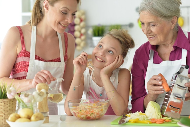 Cute girl with mother and grandmother preparing delicious fresh salad