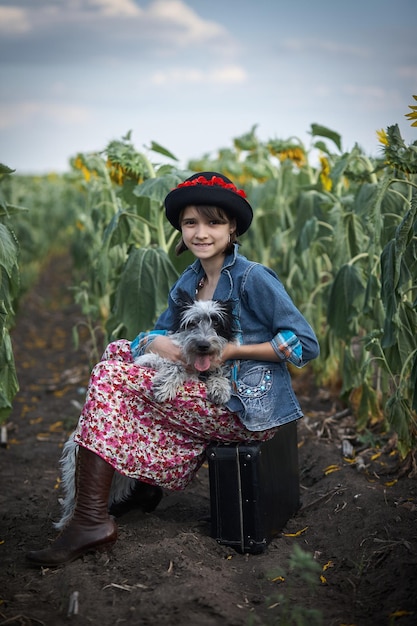 Cute girl with old suitcase and dog in a sunflower field