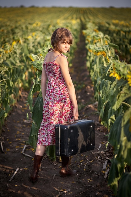 Ragazza carina con la vecchia valigia in un campo di girasoli