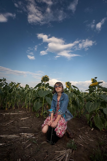 Ragazza carina con la vecchia valigia in un campo di girasoli