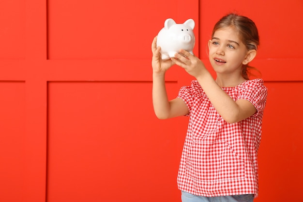 Cute girl with piggy bank on color