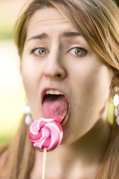 Photo cute girl with pigtails licking twisted red lollipop